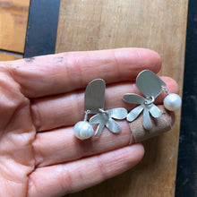 Load image into Gallery viewer, Door and Flower Sterling Silver Post Earrings with White Pearl being held in a hand above wood block